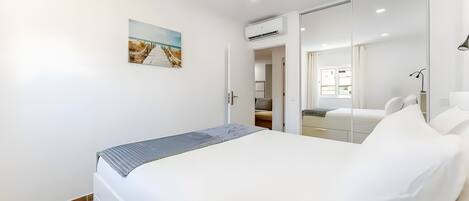 A modern bedroom with a bed, a painting, an air conditioning unit, and a mirror.