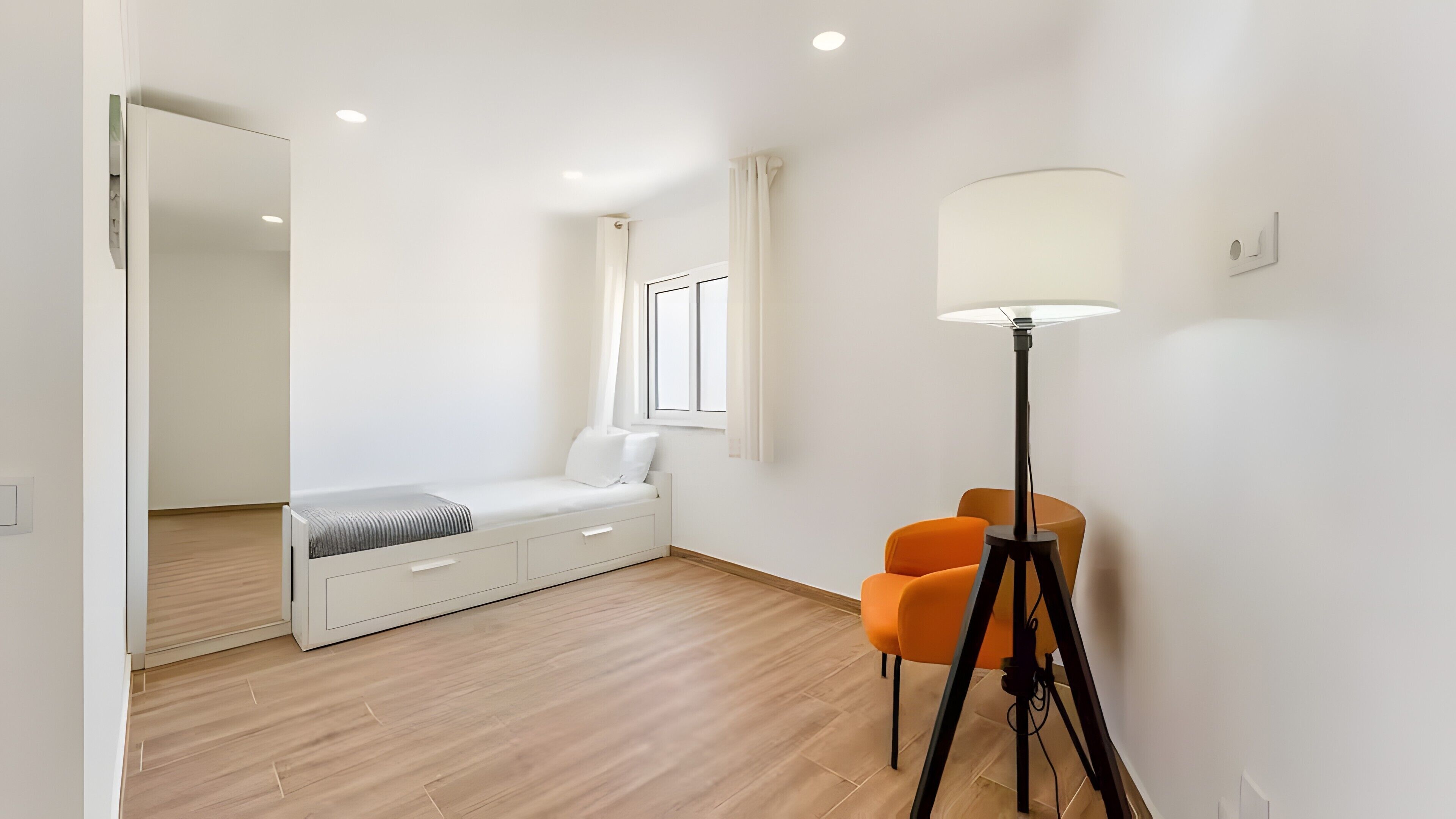 Een slaapkamer met een bed, nachtkastje, lamp en twee stoelen.