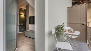 A modern interior with a glass door leading to a balcony, a small seating area with a table and chairs, and a television mounted on the wall. - GuestHost - Vivaldi Primavera Apartment (Treviglio)