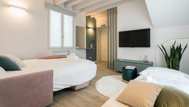 A modern bedroom with two beds, a flat-screen TV, a bedside table, and a large window. - GuestHost - Vivaldi Primavera Apartment (Treviglio)