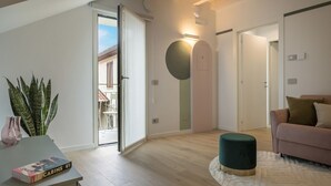 A modern living room with a sofa, a round ottoman, a coffee table with a book, and a potted plant. - GuestHost - Vivaldi Primavera Apartment (Treviglio)