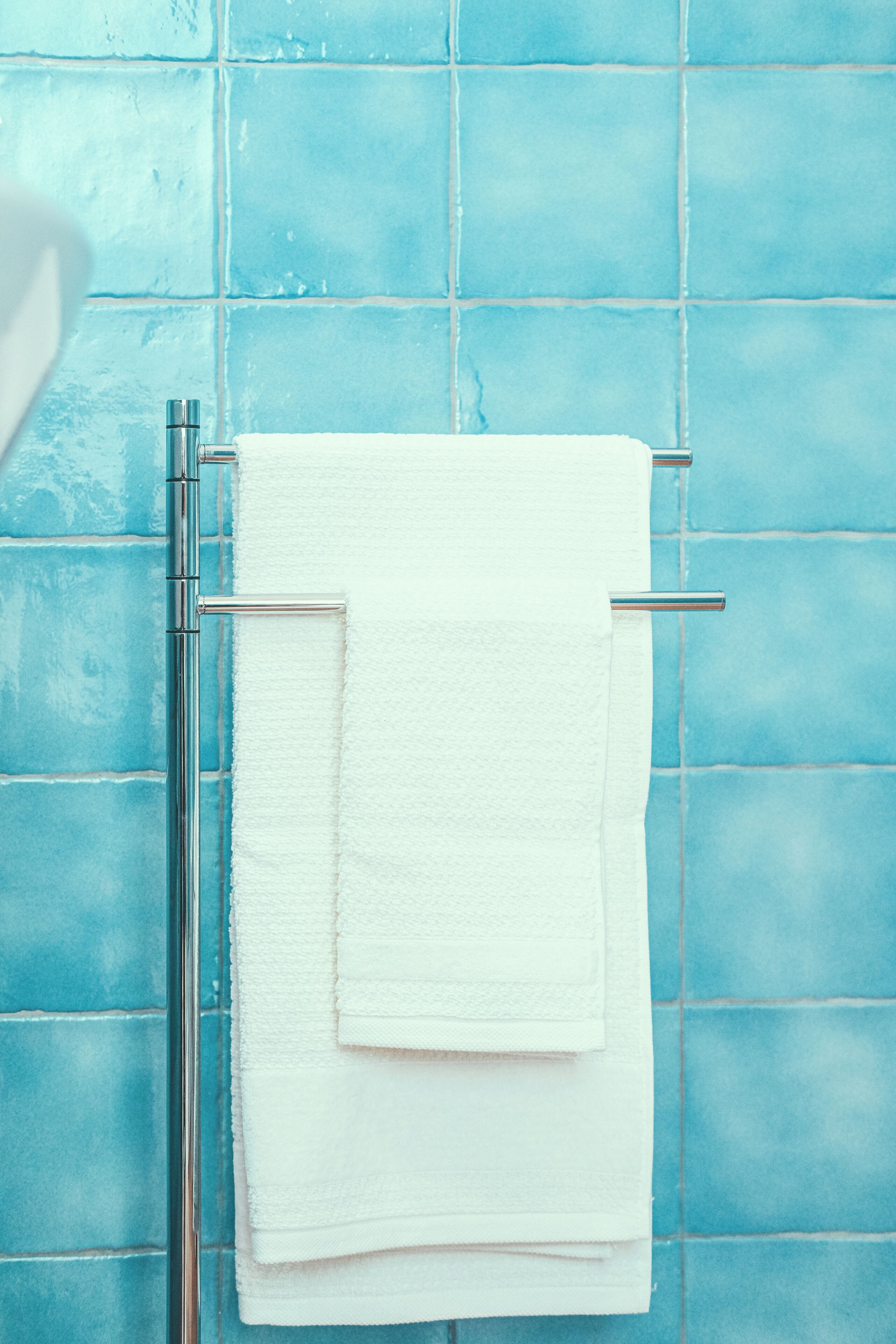 A bathroom with a white towel hanging on a metal towel rack against a blue tiled wall.