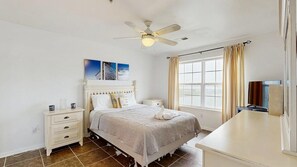 A bedroom with a bed, nightstands, a ceiling fan, a window with curtains, and a TV. - Water View Condo near Bethany Beach & Pool Access (Ocean View)
