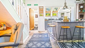 A kitchen with a bar stool, a wooden chair, a patterned rug, and a window with a view. - Hazeldene -  a cottage that sleeps 8 guests  in 3 bedrooms (Shanklin)