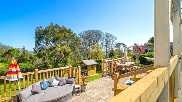 A wooden deck with a wicker sofa, a small table, and a colorful umbrella. - Hazeldene -  a cottage that sleeps 8 guests  in 3 bedrooms (Shanklin)