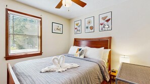 Une chambre à coucher avec un lit, un ventilateur de plafond, une fenêtre avec des stores et des œuvres d’art murales.