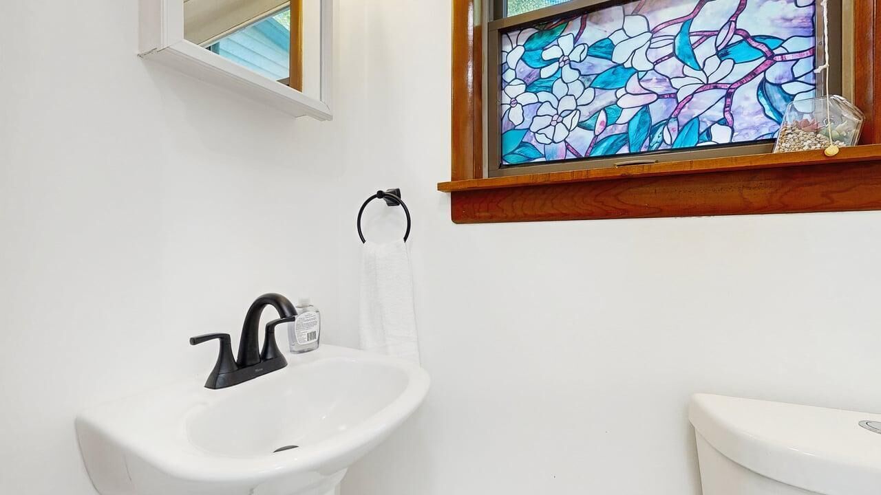 A bathroom with a white sink, black faucet, and a stained glass window above the sink.