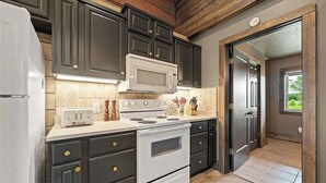 A kitchen with dark cabinets, a white microwave, a stove, and a toaster. - Barndominium Near Mt. Magazine & Lake Access (New Blaine)