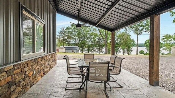 A covered patio with a stone wall, a table with chairs, and a view of the surrounding landscape. - Barndominium Near Mt. Magazine & Lake Access (New Blaine)