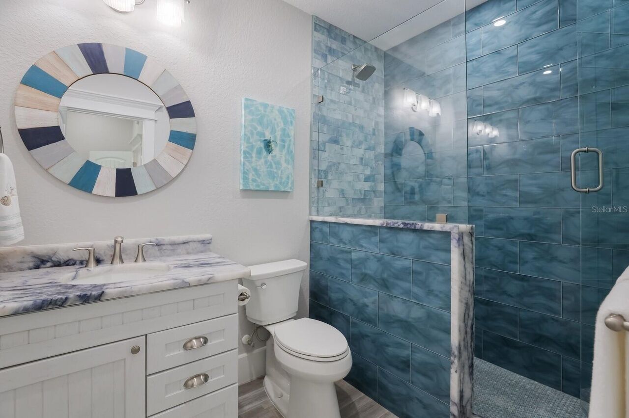 A bathroom with a marble sink, a toilet, a glass shower enclosure, and a wall-mounted mirror.