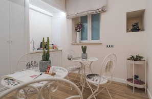 A room with a dining table, chairs, a window with a view, a shelf with decorative items, and a small plant on the windowsill. - Aurea Colosseum Guest House (Rome)