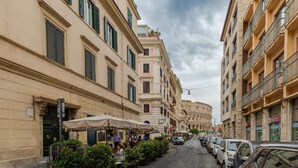 A cobblestone street lined with buildings, outdoor cafes, and parked cars.