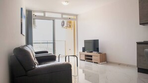 En moderne stue med sofa, fjernsyn på et træstel og en balkon med udsigt.