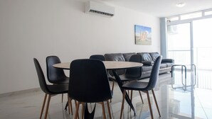 En moderne stue med spisebord, sorte stole, en grå sofa og et stort vindue.
