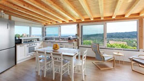 Una cocina moderna con ventanas amplias, un comedor con mobiliario blanco y vistas al campo.