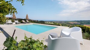 Una piscina con sillones de descanso, vistas al paisaje y un horizonte urbano distante.