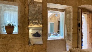 Una habitación con paredes de piedra, una cama, una ventana con una planta y vistas a un espacio exterior.