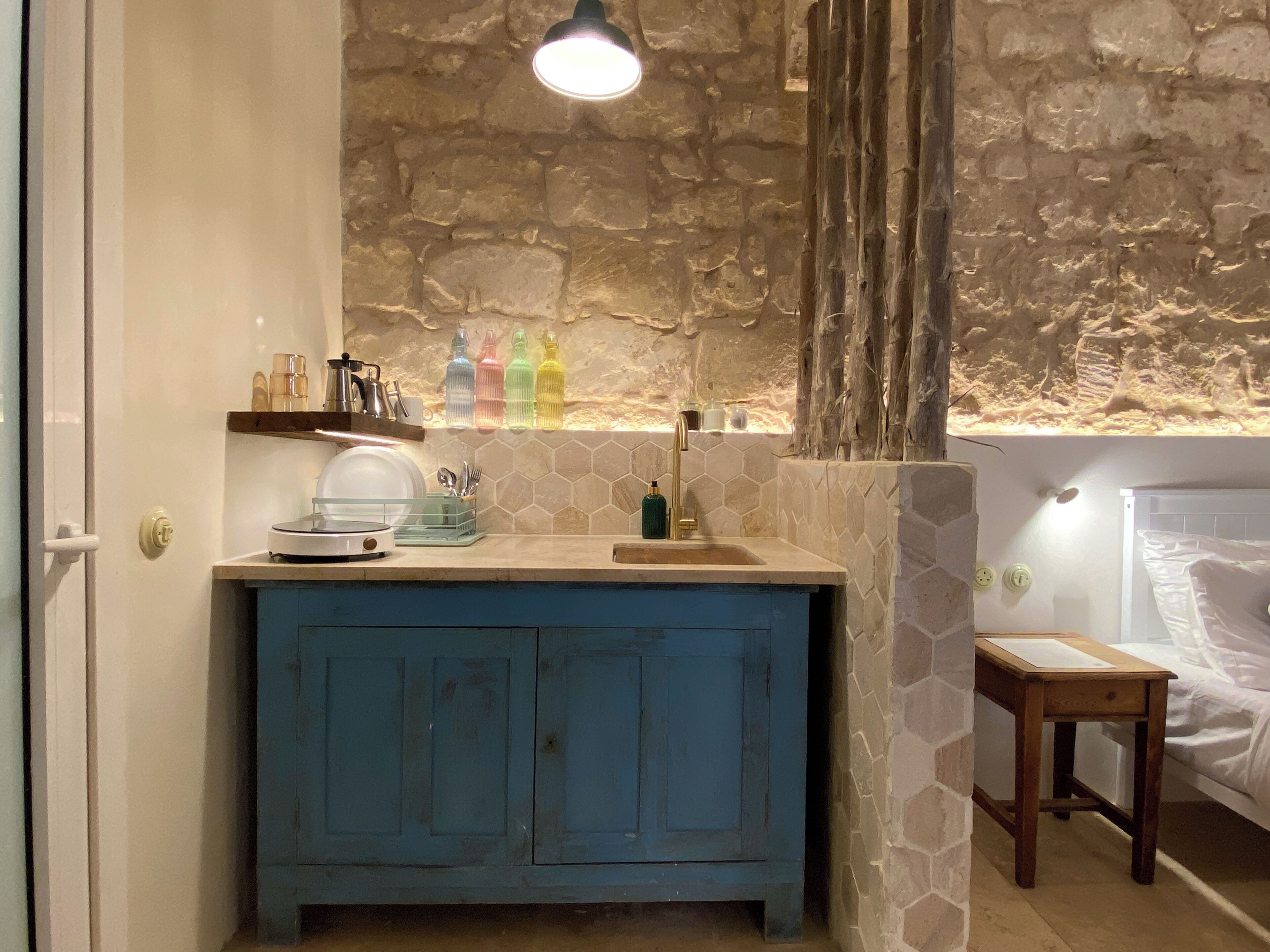 Ein Badezimmer mit Steinwand, Waschbecken, blauem Schrank und einem kleinen Holzhocker.