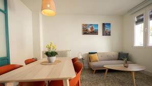 A room with a dining table, chairs, a sofa, a coffee table, a lamp, and two wall-mounted pictures.
