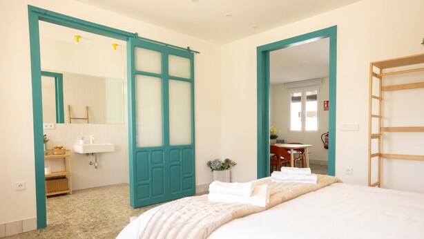 A hotel room with a bed, a bathroom with a sink, and a door leading to another room.