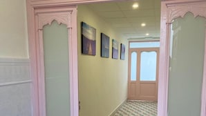A hallway with checkered flooring, a door with decorative glass panels, and framed artwork on the wall.