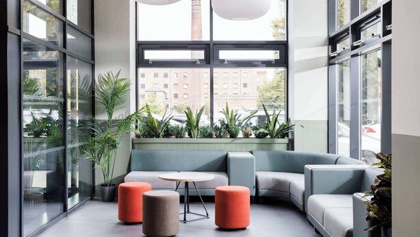 A modern interior with a sectional sofa, ottomans, a small round table, and large windows with a view of buildings and a tower.