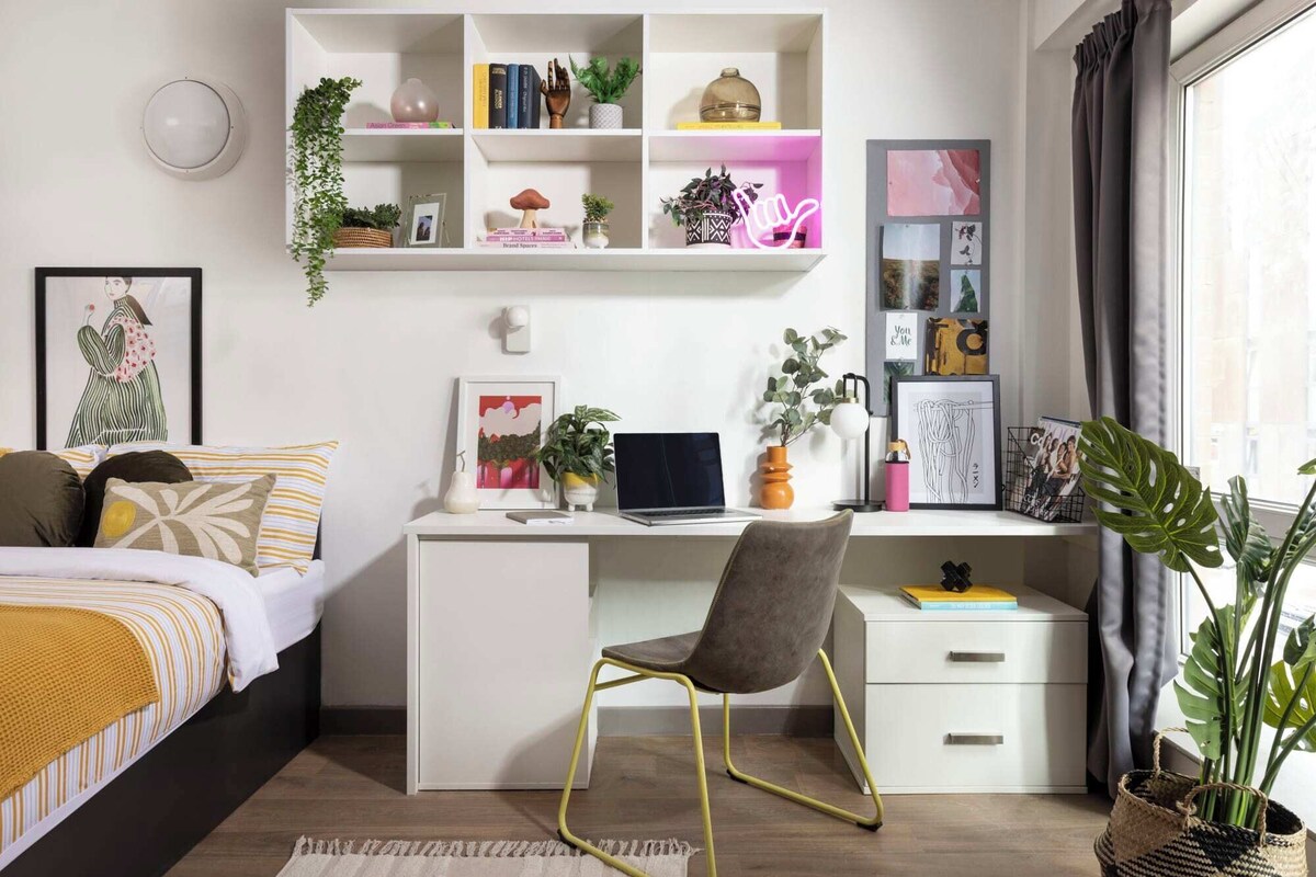 A modern bedroom with a bed, desk, chair, and shelves with books and plants.
