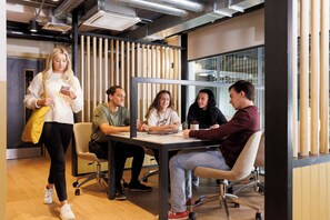 Um espaço de escritório moderno com uma mesa de reunião, cadeiras e uma pessoa parada perto da mesa.