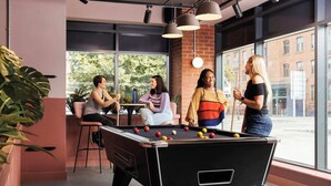 A pool table in a room with large windows, chairs, and potted plants.