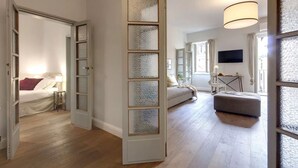 A spacious room with a large bed, a sitting area with a sofa and ottoman, a dining table, and a TV mounted on the wall. - Elegant Apartment with Terrace & Vasari Corridor Views in the Heart of Florence (Firenze)