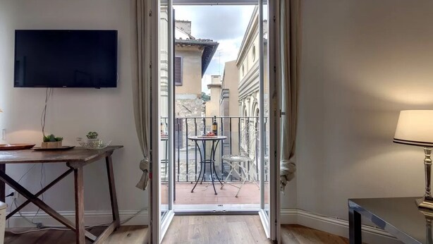 A room with a TV, a table with a plant, a balcony with a table and chairs, and a lamp. - Elegant Apartment with Terrace & Vasari Corridor Views in the Heart of Florence (Firenze)