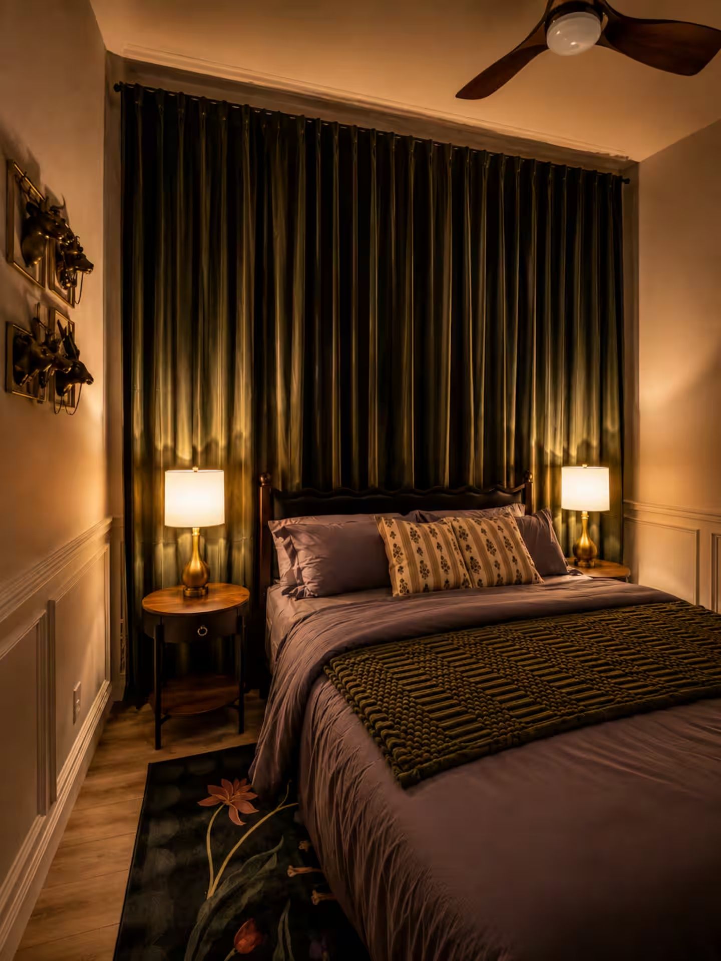 A bedroom with a bed, two bedside lamps, a ceiling fan, and a dark curtain backdrop.