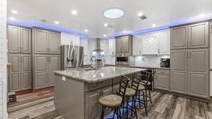 Una cocina moderna con armarios grises, una isla central con taburetes de bar, electrodomésticos de acero inoxidable e iluminación empotrada en el techo.