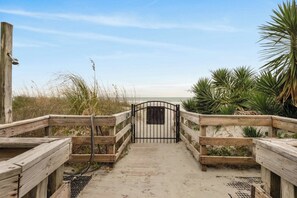A wooden boardwalk leading to a beach with a metal gate, surrounded by sand and vegetation. - Updated Pelican's Landing 308 (Myrtle Beach)