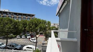 A balcony with a view of a swimming pool, parked cars, and a building in the background.