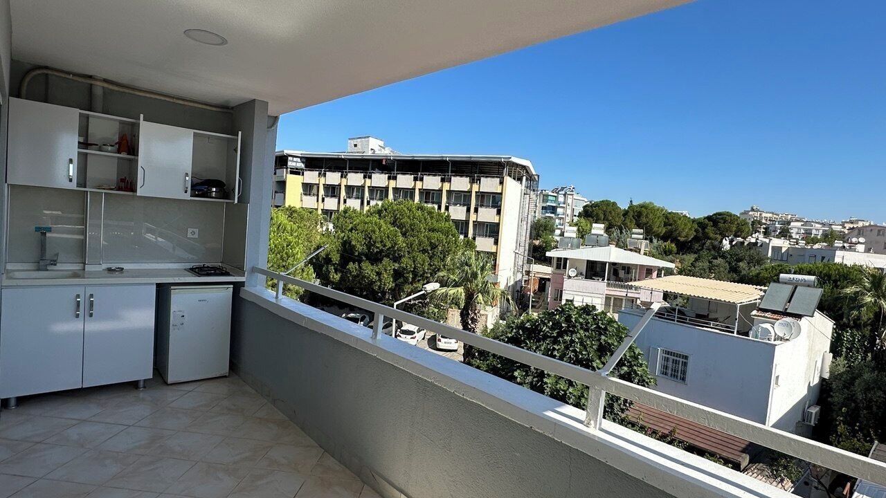 A balcony with a kitchen area, a view of buildings, and a clear sky.