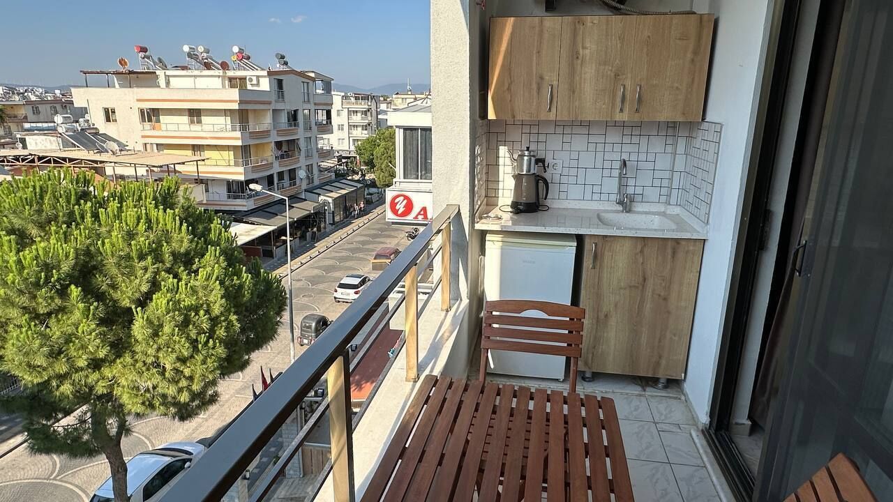 Un balcon avec un banc en bois, un petit coin cuisine comprenant un évier et des placards, et une vue sur le paysage urbain.