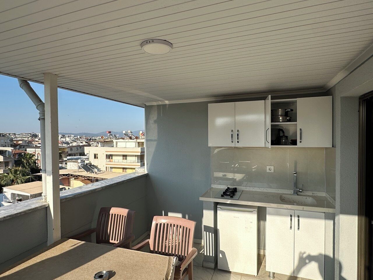A balcony with a table and chairs, a small kitchen area with cabinets and a sink, and a view of the cityscape.