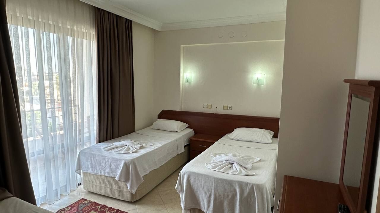 A hotel room with two beds, a large window with curtains, a wooden headboard, and a mirror.
