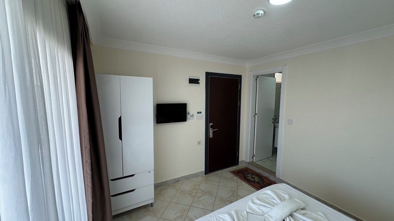 A hotel room with a bed, a wardrobe, a television, and a door leading to a bathroom.