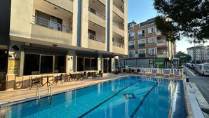 A hotel with a swimming pool, outdoor seating, and multiple balconies.