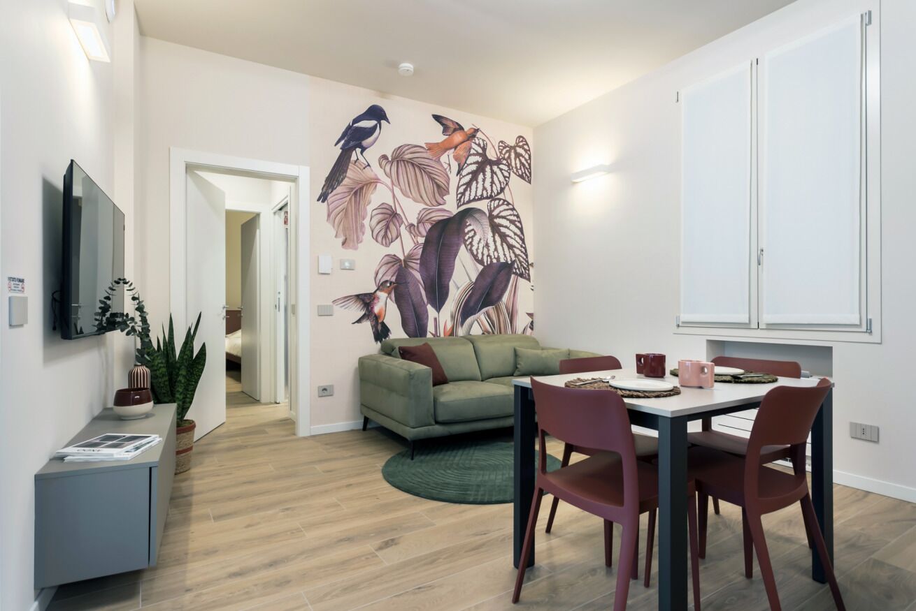 Ein modernes Wohnzimmer mit einem grünen Sofa, einem Esstisch mit Stühlen, einem Flachbildfernseher und einem Wandbild.