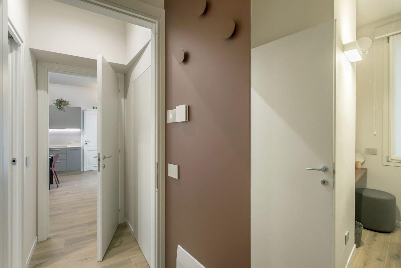 A hallway with a kitchen in the background, a brown wall with circular decorations, and a grey ottoman.
