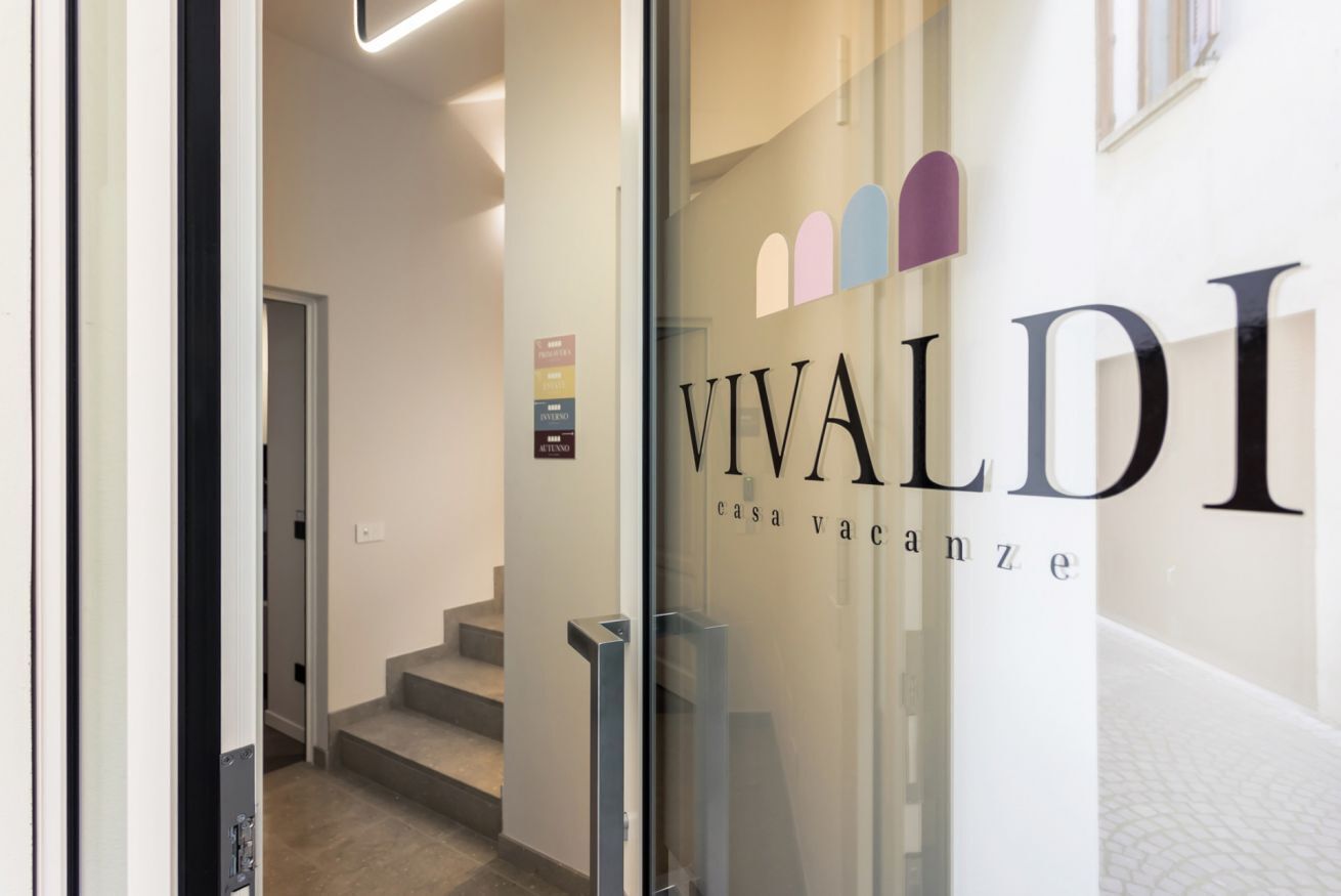 Un couloir avec une porte en verre sur laquelle on peut lire : « VIVALDI casa vacanze ».