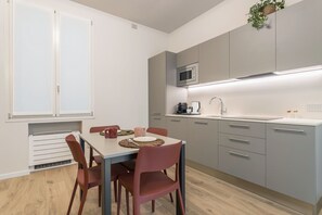 A modern kitchen with grey cabinets, a microwave, and a sink. There is a dining table with chairs and a plant hanging above it.