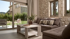 Ein modernes Wohnzimmer mit Steinwand, einer Sofagarnitur, einem Couchtisch und Blick auf ein Steinhaus sowie Grünflächen im Freien.