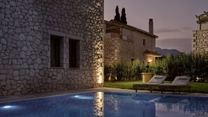 Ein Steinhäuschen mit Pool, Liegestühlen und einem gepflegten Garten.