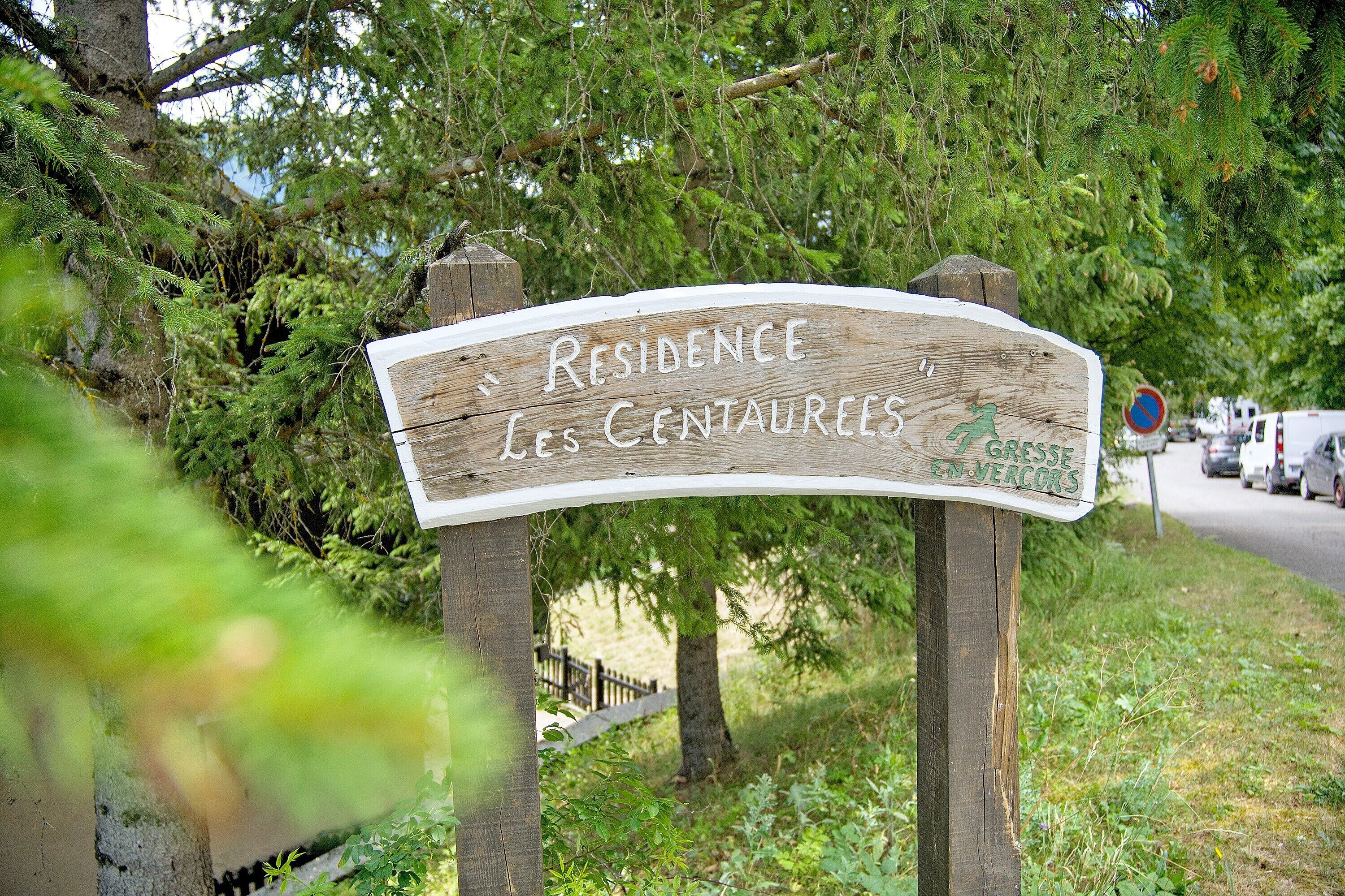 Un cartello in legno con la scritta 'Résidence Les Centaurees' che indica una zona residenziale.