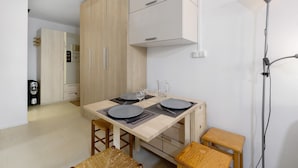 A compact kitchen with wooden cabinets, a dining table set for two, and a modern floor lamp.