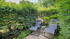 A garden with two lounge chairs and a small table, surrounded by dense foliage.